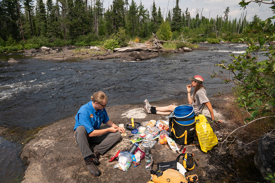 A guide and customer sit on a boulder and enjoy a typical shore lunch from Wabakimi Outfitters