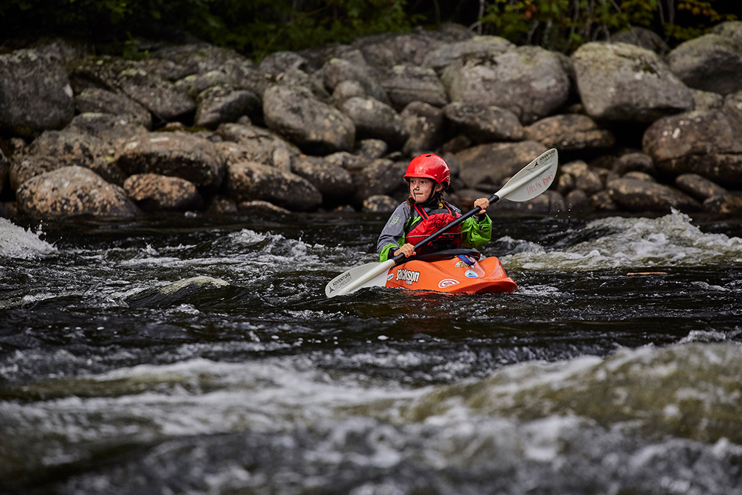 a young whitewater kayaker paddles on a rocky river