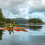 Kayaks For Her: What To Know When Buying A Women’s Kayak woman paddling a kayak on a scenic lake under clouds