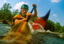 man paddling a whitewater boat and dipping his paddle into the water near the camera