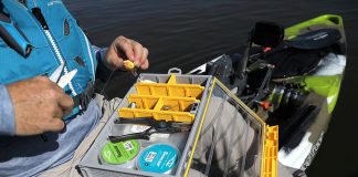 angler sits on his kayak and rigs up his fishing line with a lure