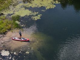 overhead photo of a man standing and fishing on shore beside his paddleboard
