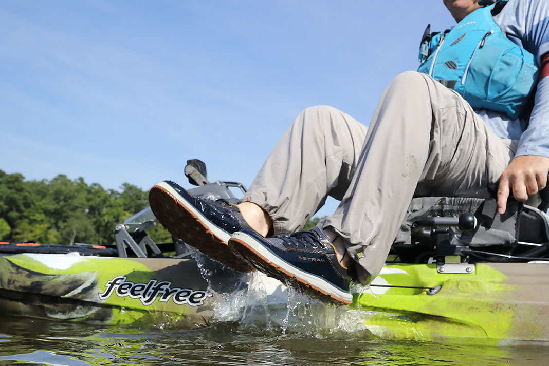 kayak angler lifts his fishing shoes out of water while sitting on the kayak