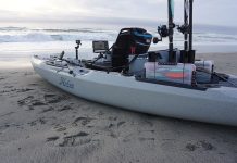 a kayak sits on the beach by the surf with organized fishing tackle in the stern