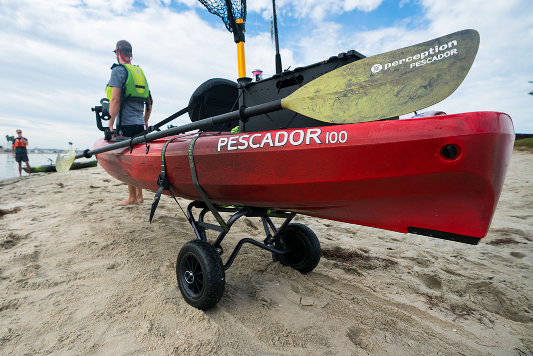 man pulling a Perception Pescador 10 on a kayak cart along a sandy beach to the water