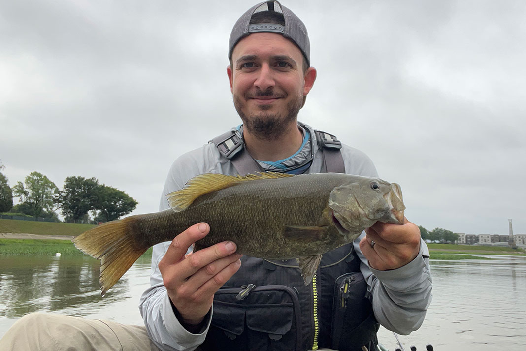 kayak angler holds up smallmouth bass in front of cloudy skies