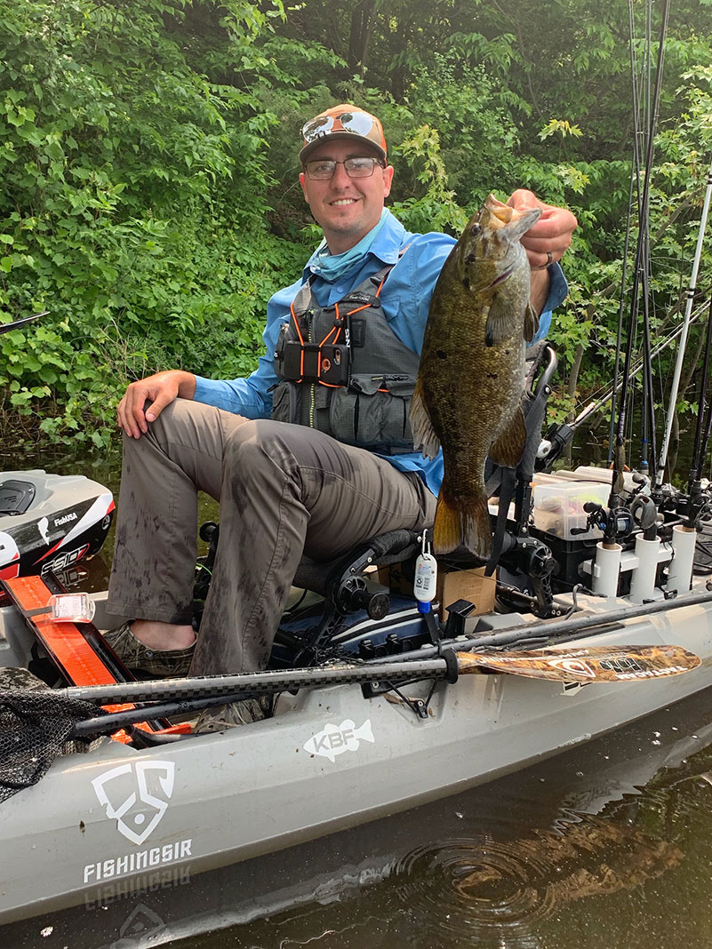 man smiles as he holds up a smallmouth bass caught by kayak in its native range