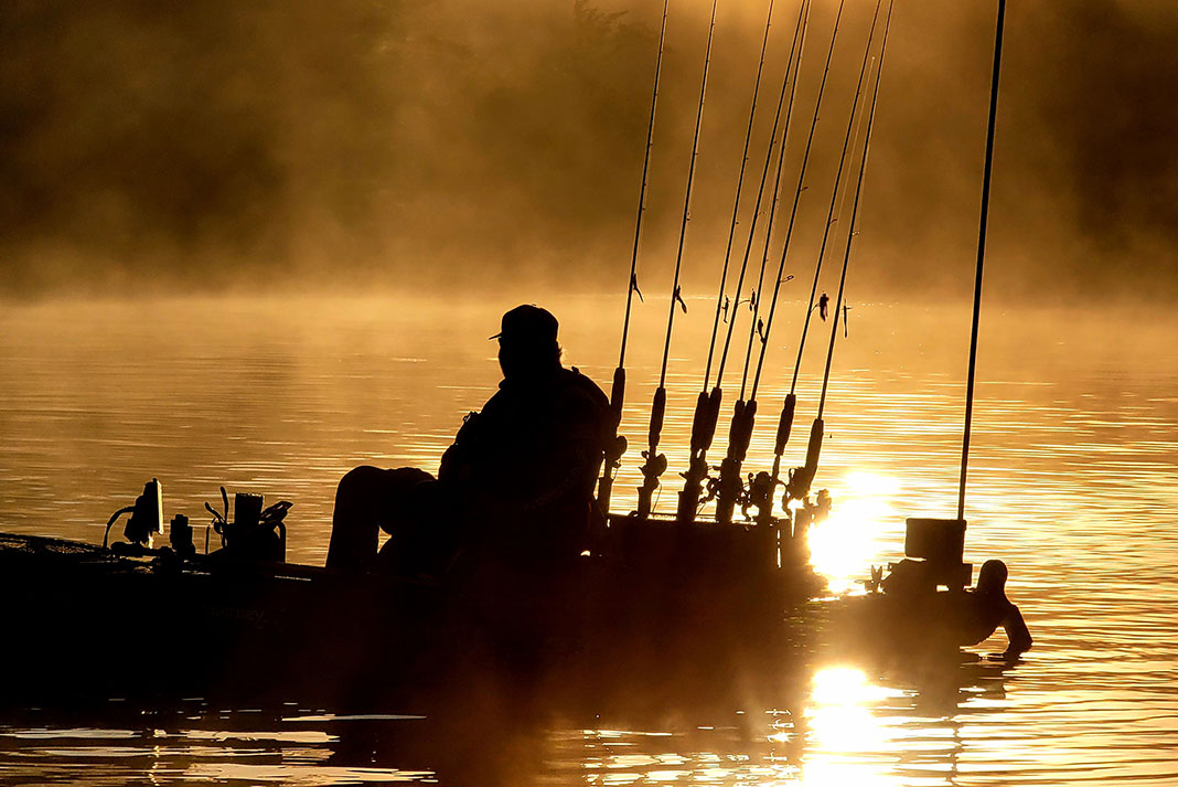 person silhouetted on the misty morning water in a fully rigged fishing kayak