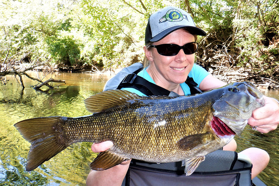 woman holds up a smallmouth bass she caught while kayak fishing