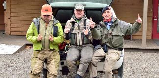 three anglers tell tall tales about the size of a fish while leaning against the trunk of a vehicle