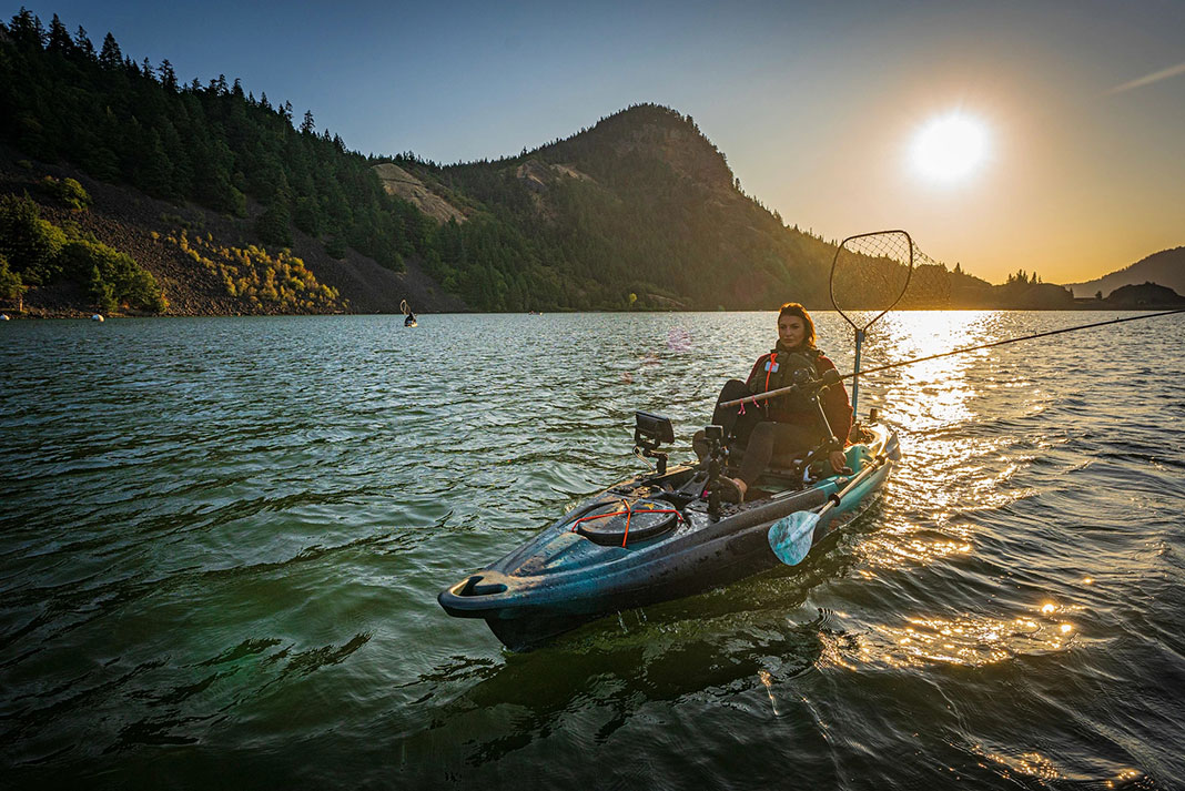 woman outfitted with large fishing net kayaks with a partner in front of mountains and late afternoon sun