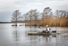 man paddles the Ascend 12T fishing kayak past some waterlogged trees and grasses in fall
