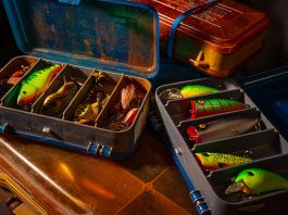 two tackle boxes filled with fishing lures sit opened on a countertop f