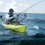 man fishes open water from a kayak rigged for ocean fishing