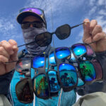 Best Fishing Sunglasses For 2026 kayak angler with gaiter poses with a selection of different fishing sunglasses