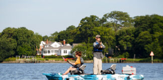 Best Tandem Fishing Kayaks For 2026 man stands and casts his fishing rod while woman sits and paddles the Feelfree Lure II tandem fishing kayak