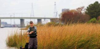 Ultimate Rigging Guide For Kayak Safety Gear Kayak Angler editor Ric Burnley stands and fishes from a kayak near grass flats with a bridge behind