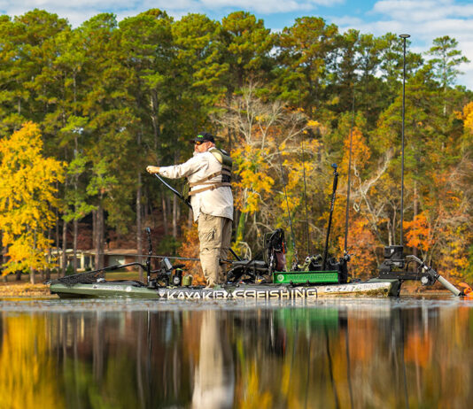 Chad Hoover stands and paddles while passing trees on the shore