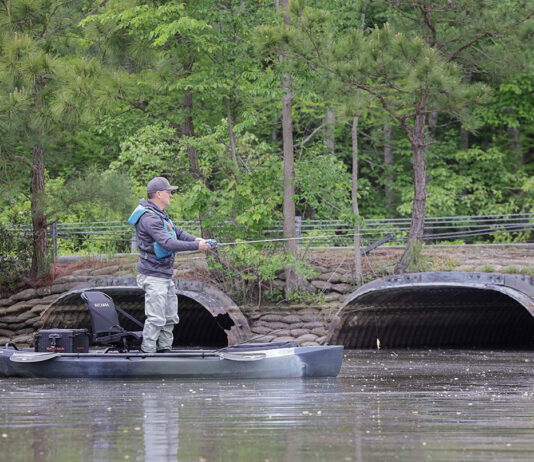 man stands and fishes from the NuCanoe Unlimited U10 compact fishing kayak near a low bridge