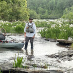 3 Experts On What Makes A Great River Fishing Kayak man wades down a river with his fishing kayak