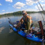 man holds up a large bass caught by kayak while fishing a with a bass rig
