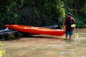 Man launching tandem kayak on lake.