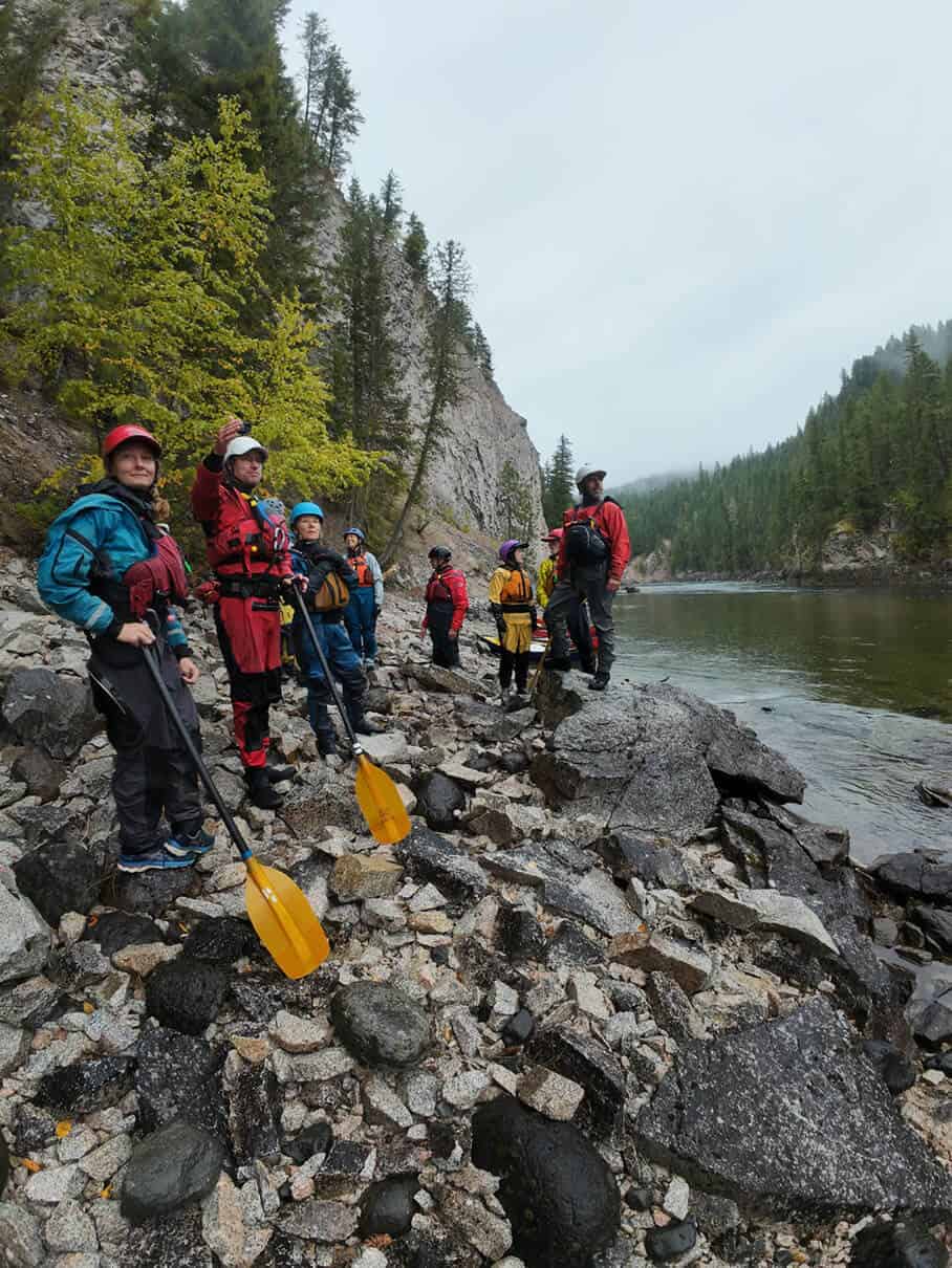 a group of canoeists stand on a rocky riverbank scouting the way ahead during the 4 Rivers In 4 Days trip by Elements Adventure Company
