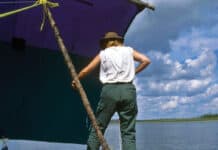 person stands on a canoe rigged up as part of a catamaran with canoe sail