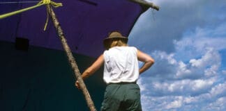 person stands on a canoe rigged up as part of a catamaran with canoe sail