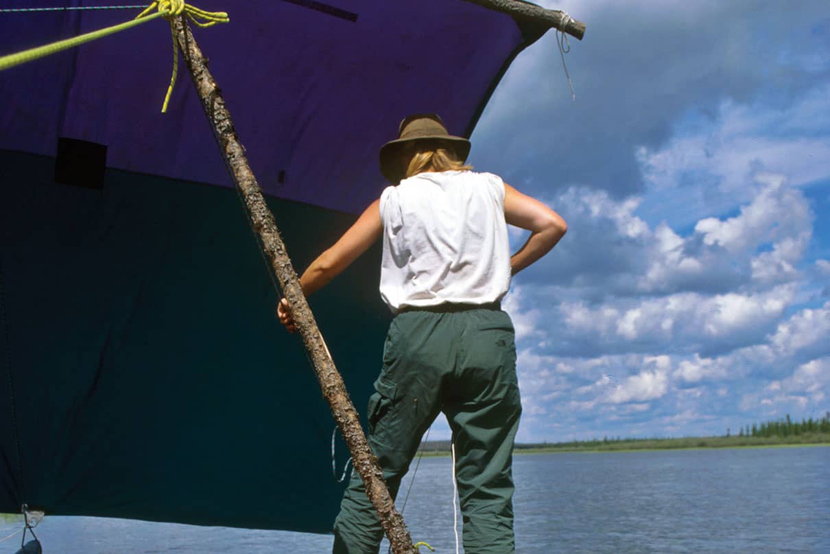 person stands on a canoe rigged up as part of a catamaran with canoe sail