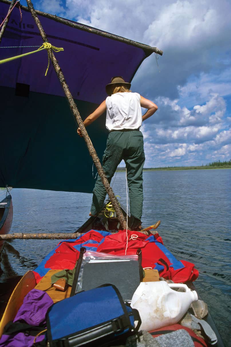 person stands on a canoe rigged up as part of a catamaran with canoe sail