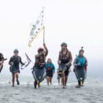 Paddle Tribal Waters youth carry a tribal flag at the mouth of the Klamath River on June 11