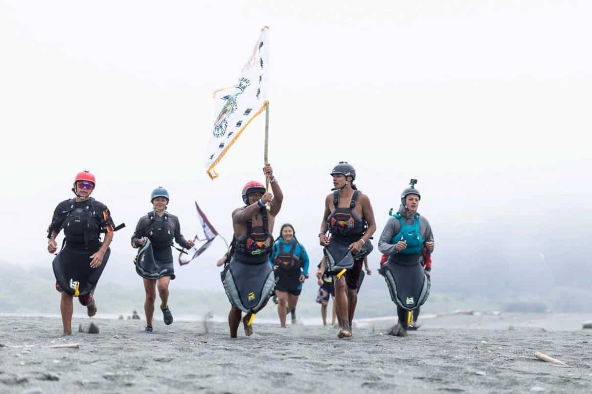 Paddle Tribal Waters youth carry a tribal flag at the mouth of the Klamath River on June 11