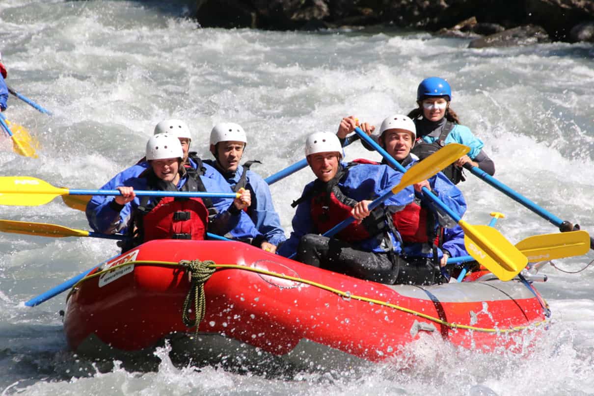 Six people in a red raft paddle through rapids on the Illecillewaet River.