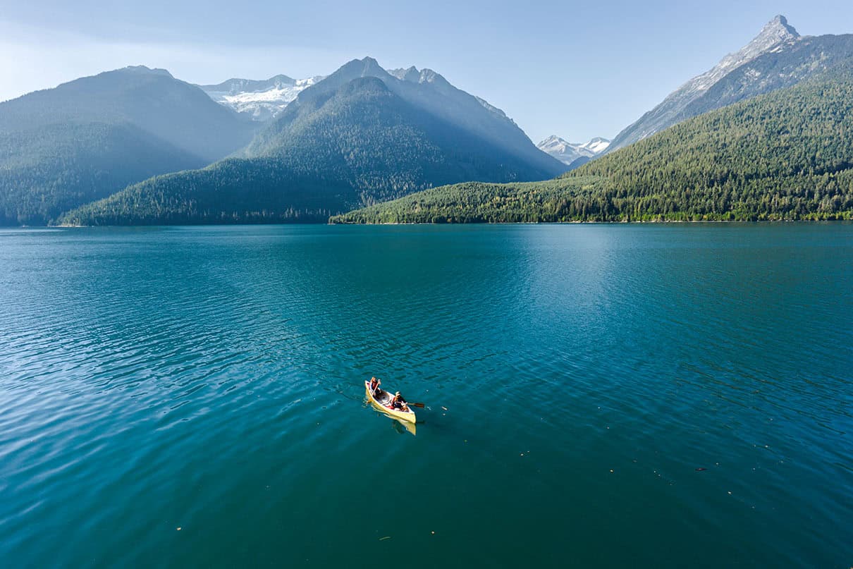 A yellow canoe floats on Lake Revelstoke with mountains in the background.