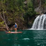 A paddleboarder stands next to a waterfall