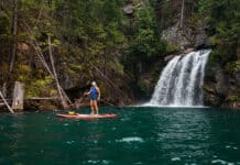A paddleboarder stands next to a waterfall