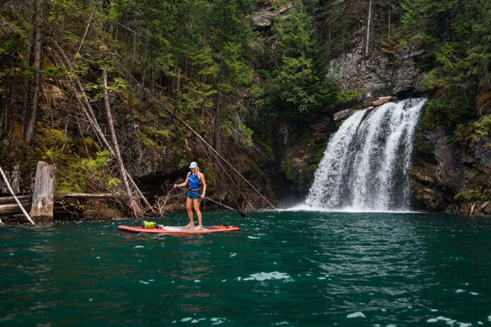 A paddleboarder stands next to a waterfall