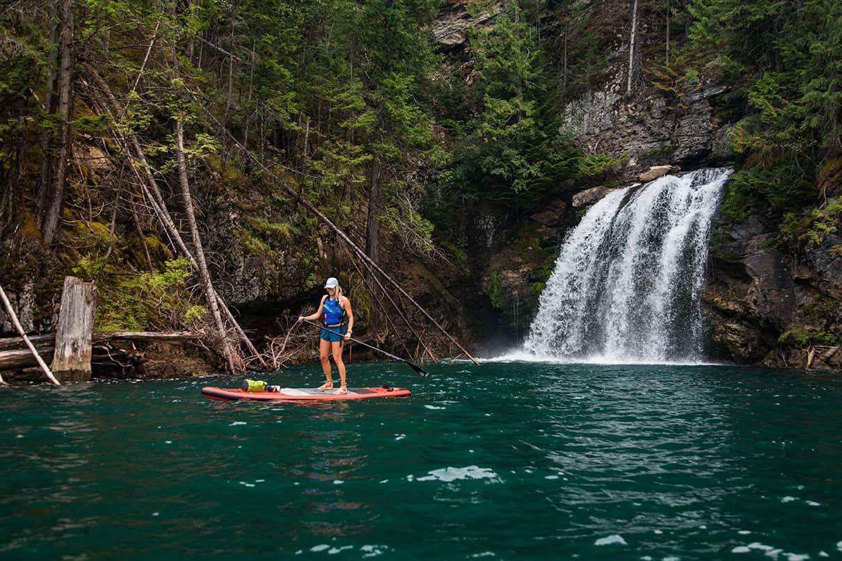 A paddleboarder stands next to a waterfall