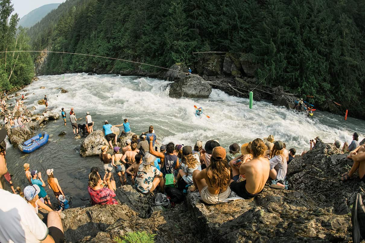 People gathered at rocky edge of river to watch whitewater paddles at Revy Paddle Fest.