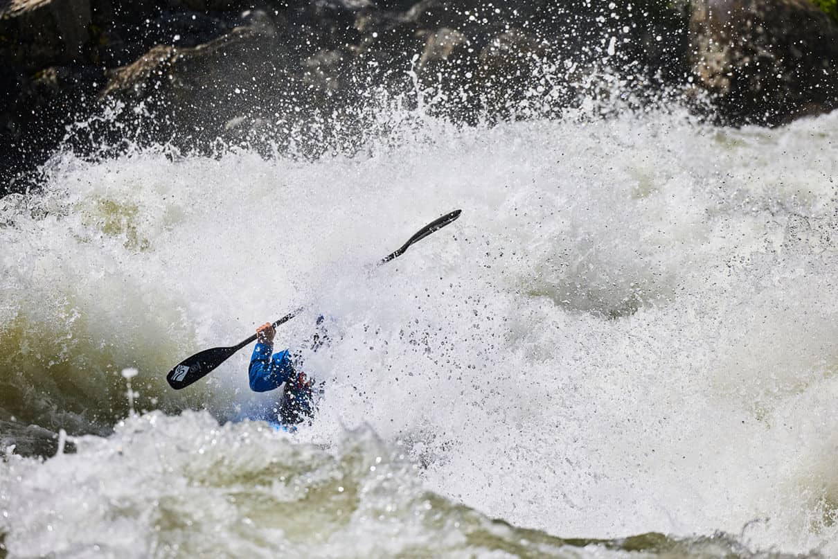 a person paddles through roaring rapids