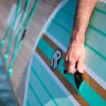 close-up of a man holding the grab handle on an inflatable SUP while carrying it