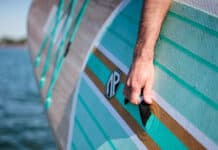 close-up of a man holding the grab handle on an inflatable SUP while carrying it