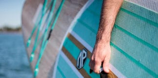 close-up of a man holding the grab handle on an inflatable SUP while carrying it