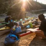 two people pack their kayaks in the sun while kayak camping