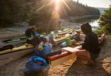 two people pack their kayaks in the sun while kayak camping
