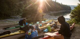 two people pack their kayaks in the sun while kayak camping