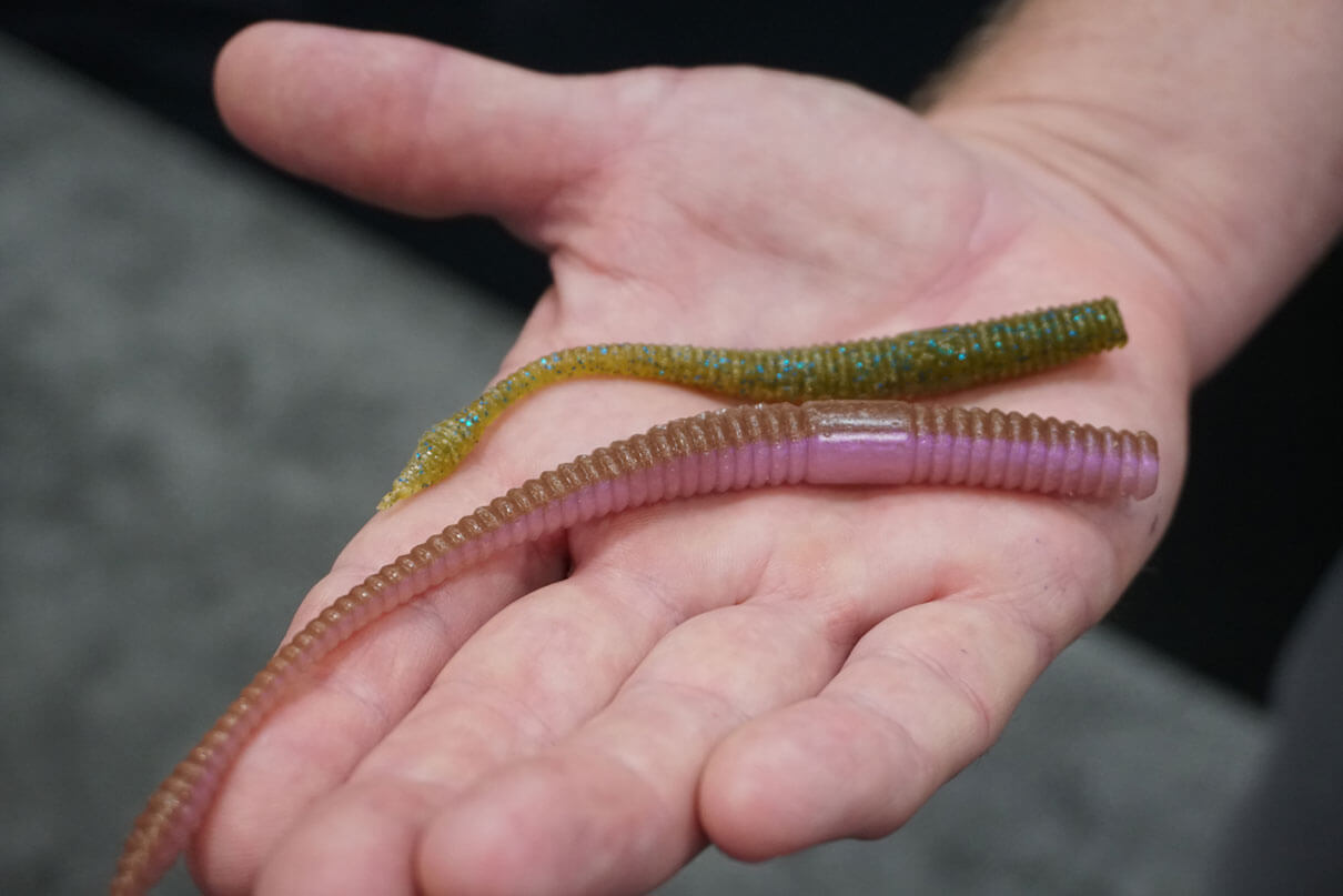 two Lunkerhunt soft plastic lures are displayed on the palm of a person's hand at ICAST 2025