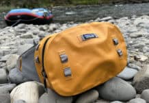 The Patagonia Guidewater waterproof hip pack sitting on rocks near the edge of a river with a raft in the background.