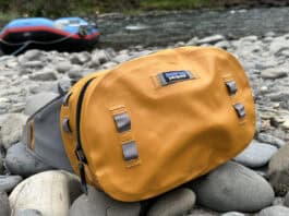 The Patagonia Guidewater waterproof hip pack sitting on rocks near the edge of a river with a raft in the background.